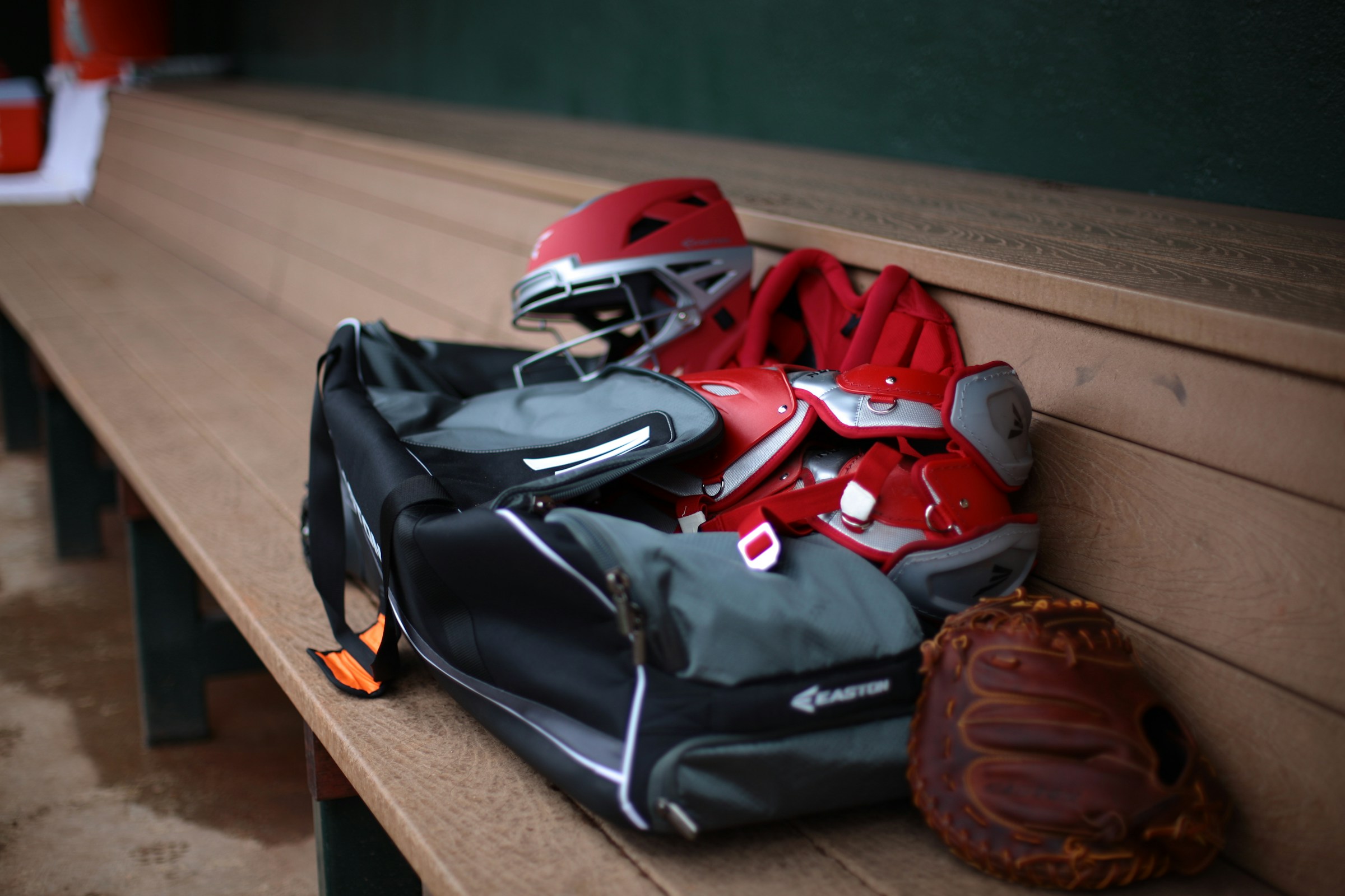 Baseball glove, catcher's mitt, and batting helmet on a bench beside a gear bag