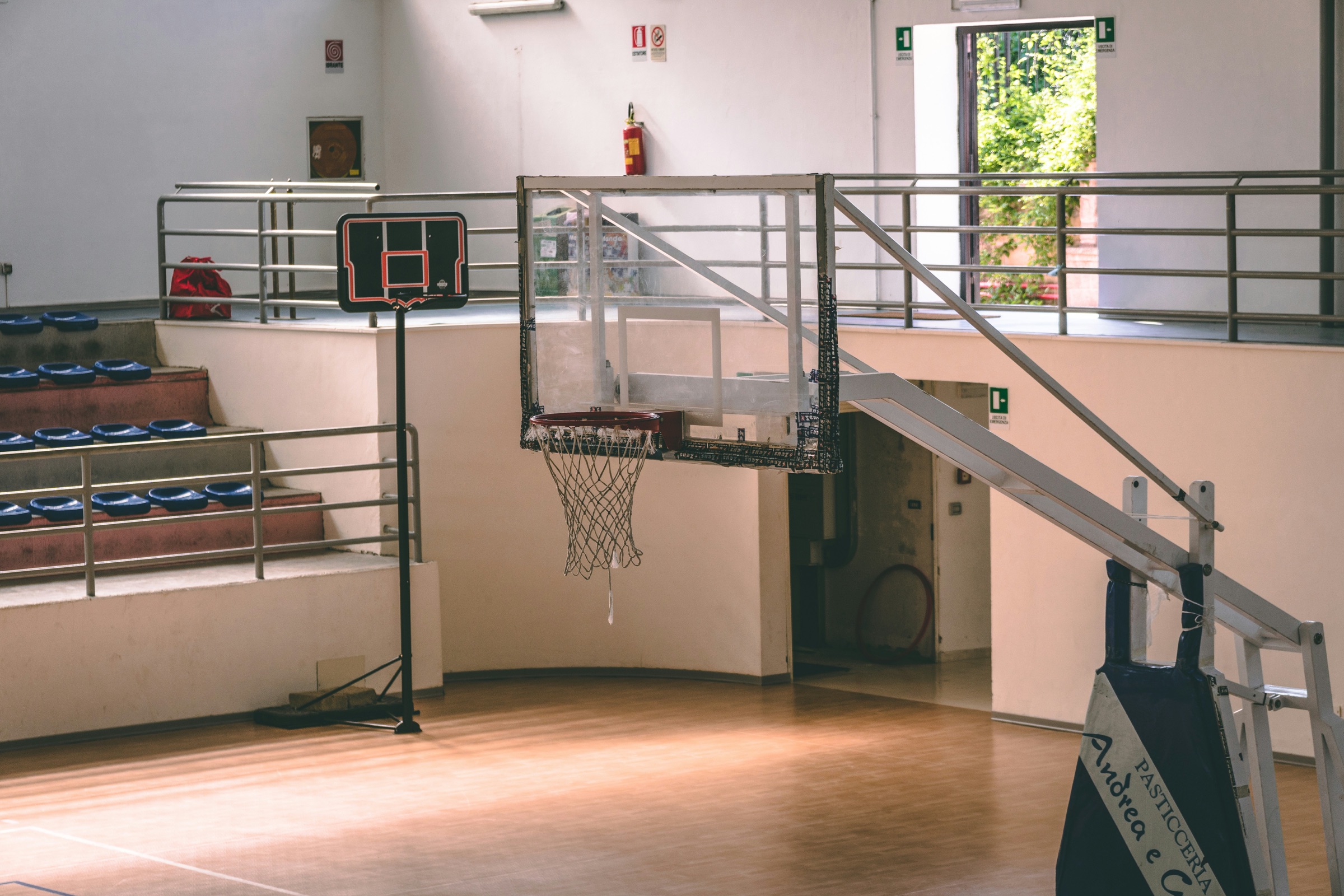 Indoor basketball gym with a mobile hoop, wooden court, and stadium seating
