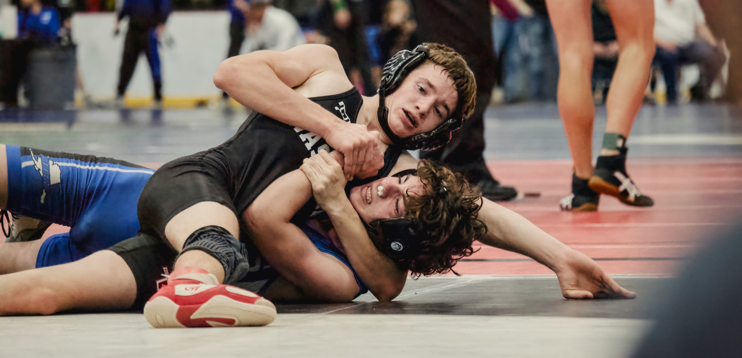 Two high school wrestlers grappling during a tournament match on a red and black mat